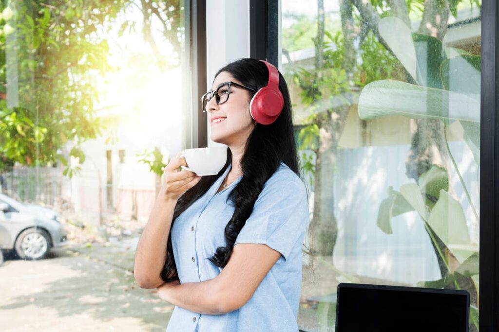 Femme souriante qui est dehors avec son casque sur les oreilles et une tasse de café en mains