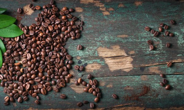 Photo de grains de café étalés sur une table en bois décapée.