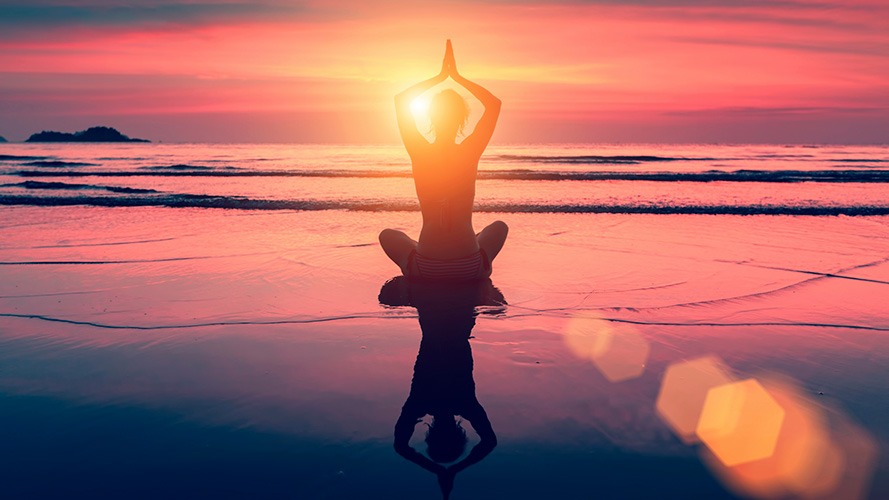 Photo d'une personne sur la plage devant un coucher de soleil en train de méditer