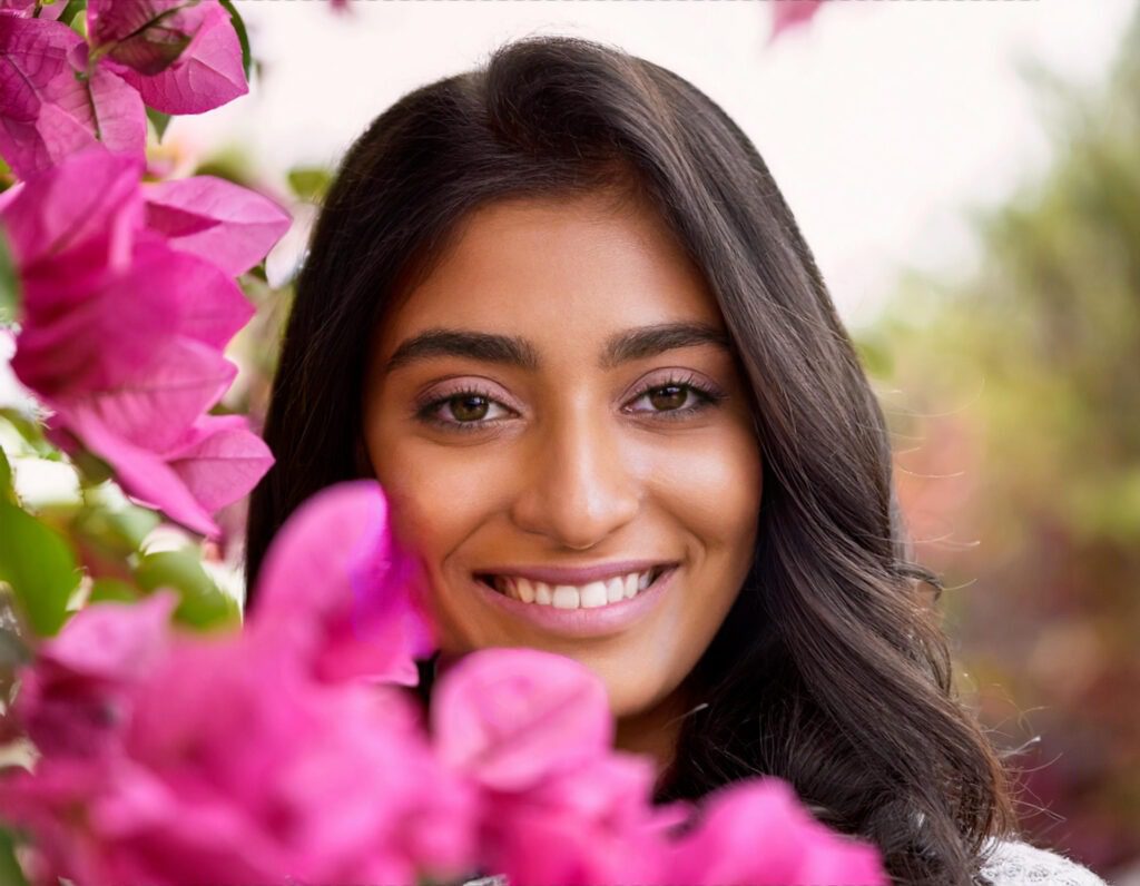 Photo d'une femme indienne souriante derrière des fleurs rose fushia