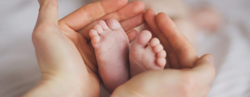 Photo représentant des mains de femmes tenant en leur centre les pieds d'un nouveau né