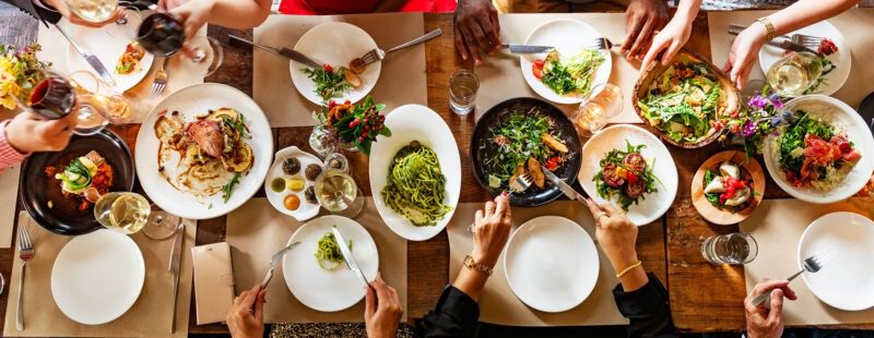 AdobeStock_1290880350 Photo représentant une grande tablée avec des assiettes remplies d'aliments colorés