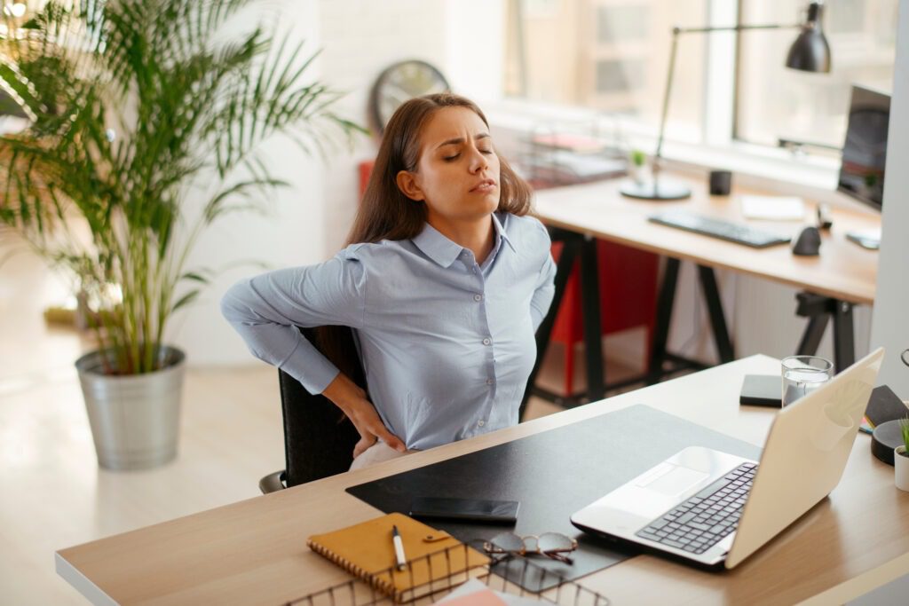Photo d'une femme derrière son bureau qui semble avoir mal au dos.