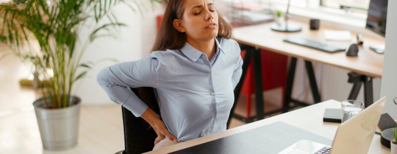 Photo d'une femme derrière son bureau qui semble avoir mal au dos.